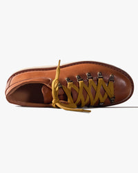 Brown leather shoe viewed from above, with yellow laces on a white background