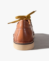 Brown leather shoe viewed from rear, with heel facing, yellow laces on a white background